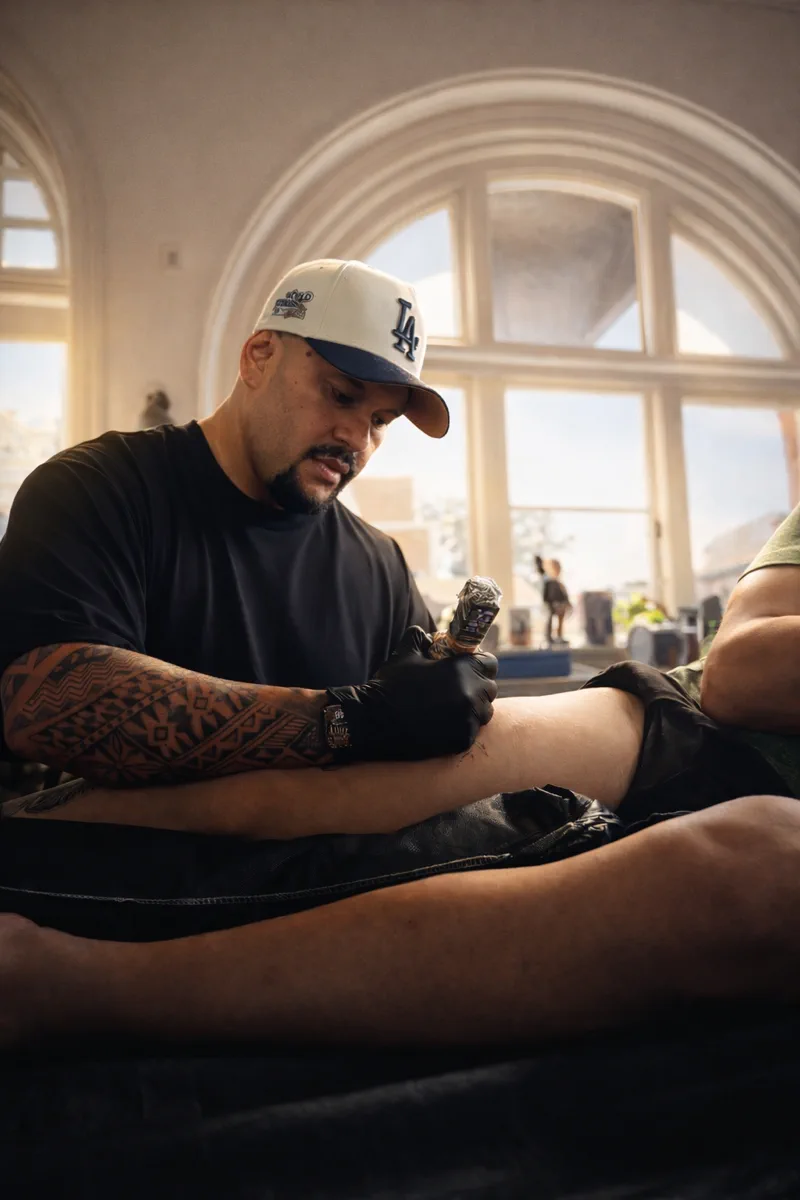 Ameo tattooing a client's leg in the studio under bright natural light